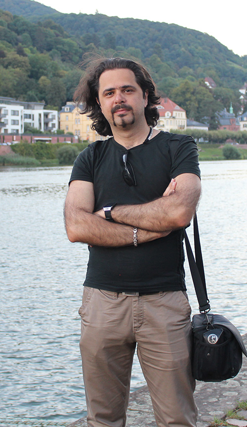 Kaveh Bakhtiyari standing by a river with wooded hills behind him